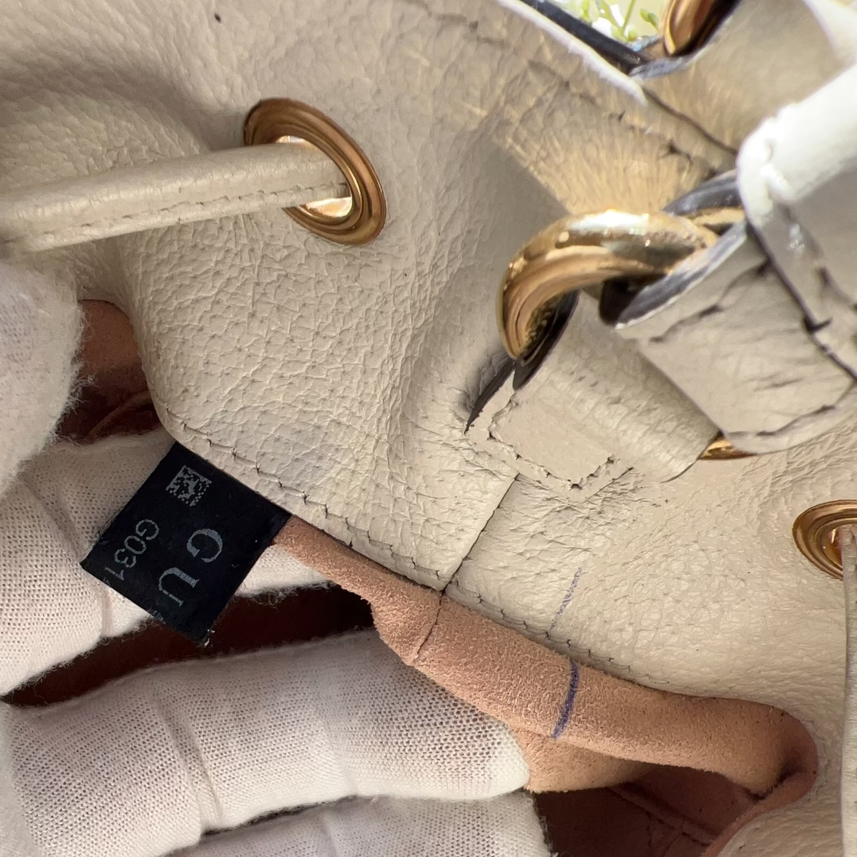 Close-up of a beige handbag with gold hardware and a visible Gucci tag.