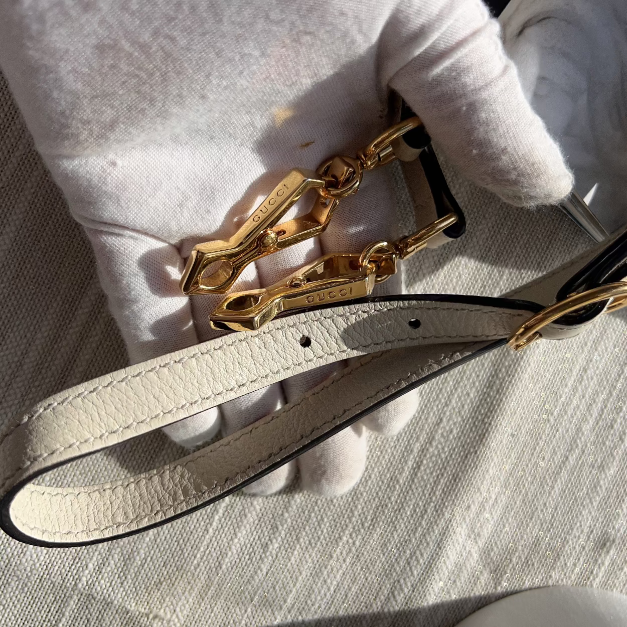 Close-up of a gold clasp on a beige leather strap with a blurred background