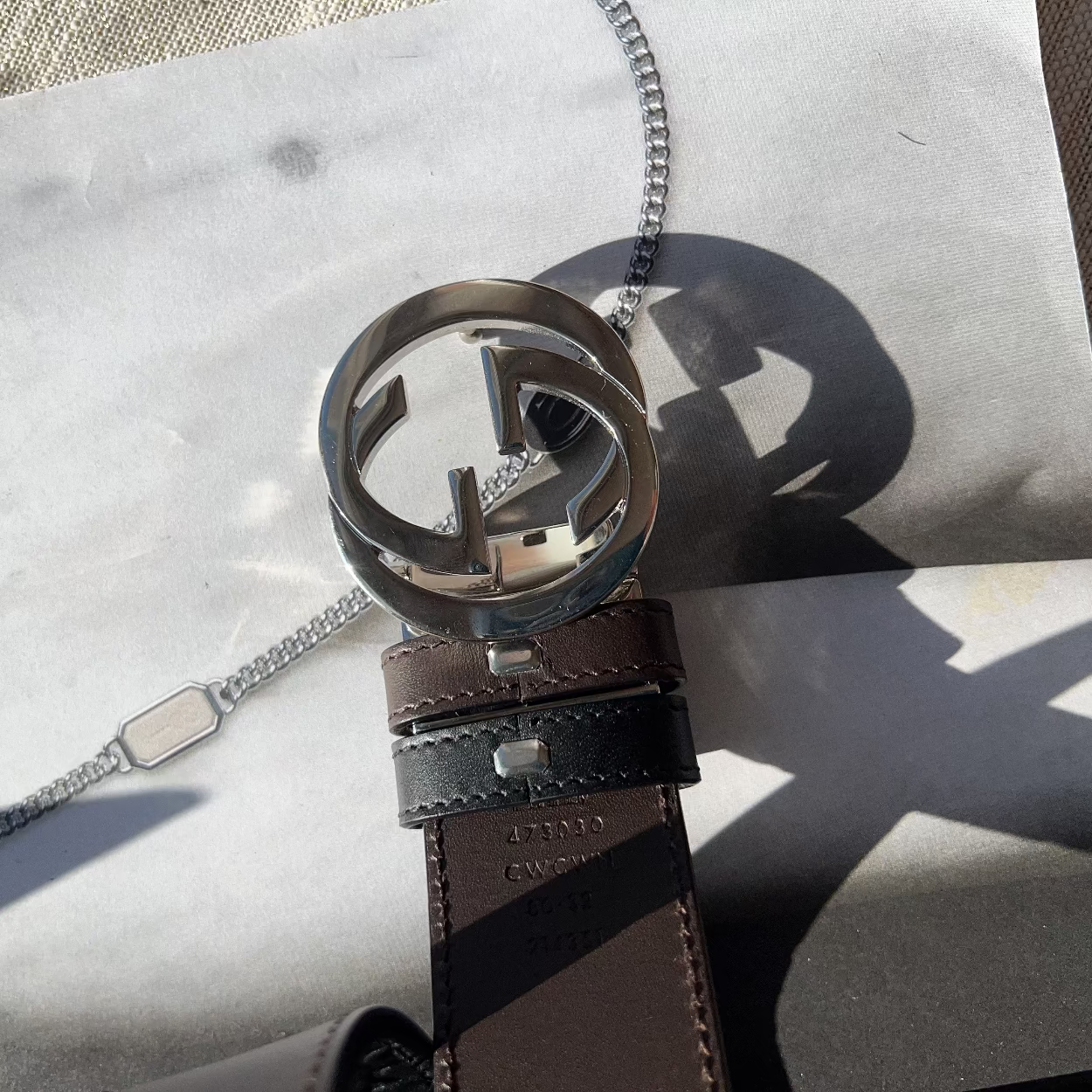 Brown leather belt with silver Gucci buckle on a marble surface