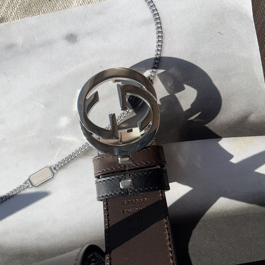 Brown leather belt with silver Gucci buckle on a marble surface