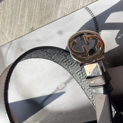 Close-up of a Gucci belt with interlocking G buckle on a textured surface.