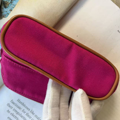 A close-up of a bright magenta pink fabric pouch with a tan leather trim, held by a white gloved hand over an open book.