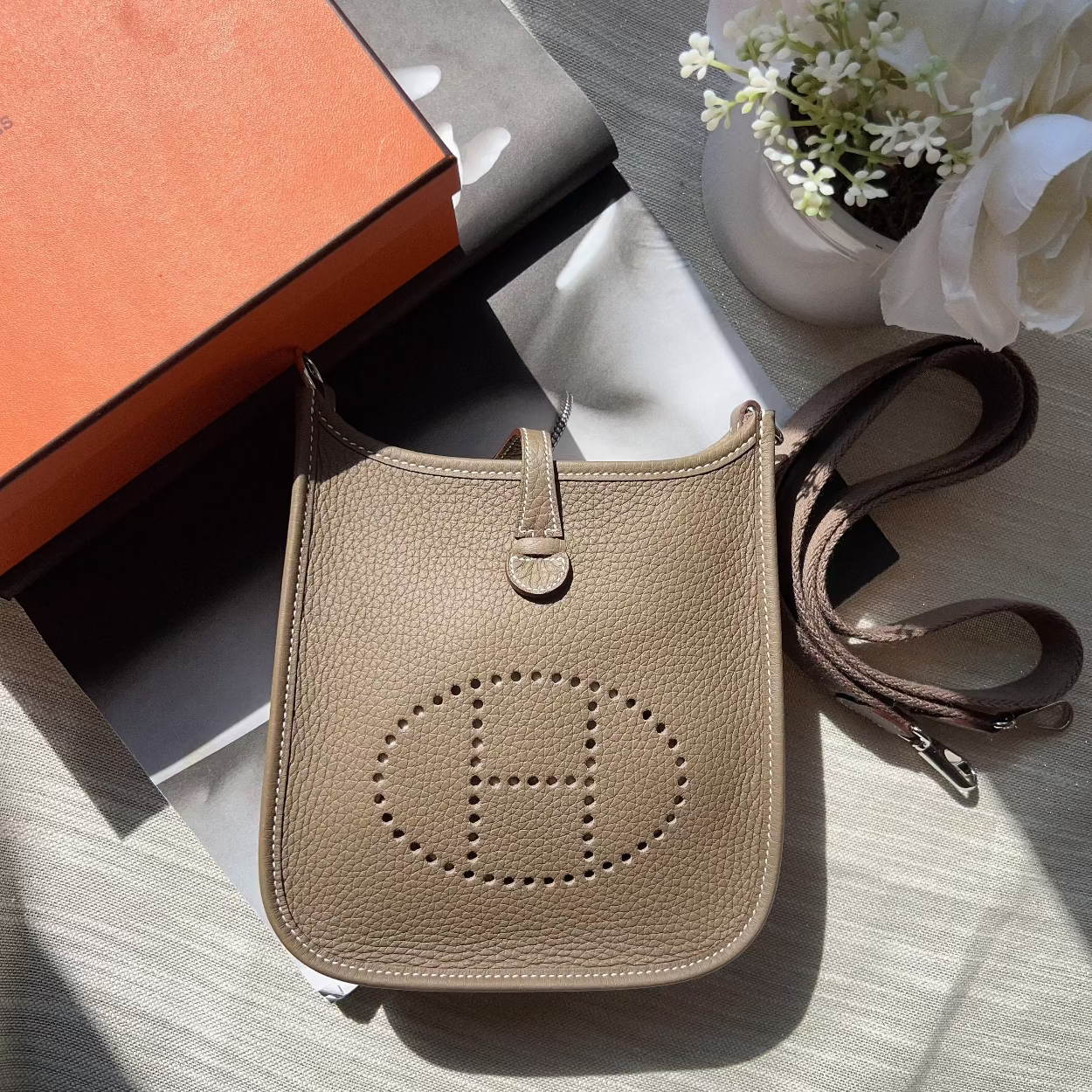 Beige handbag with brand logo on a textured surface with flowers in the background