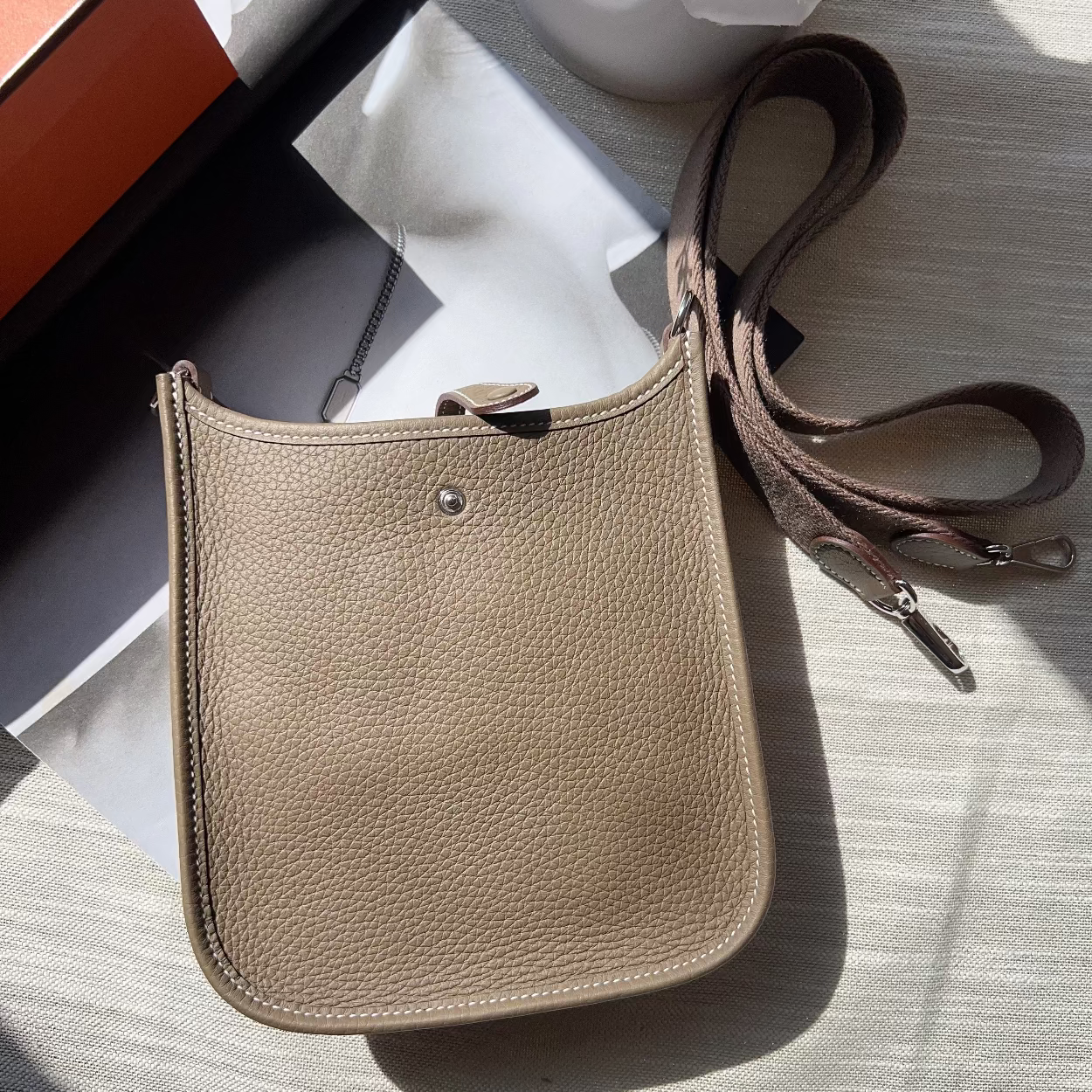Beige leather crossbody bag on a light surface with a plant in the background