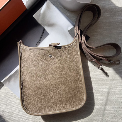 Beige leather crossbody bag on a light surface with a plant in the background