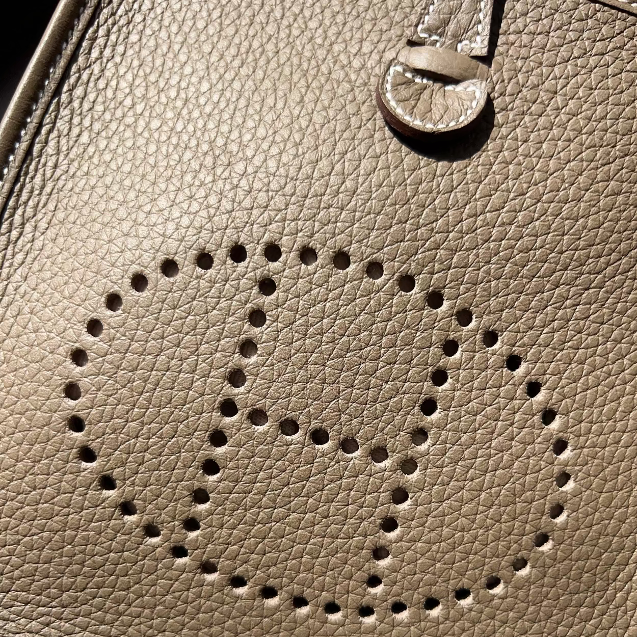Close-up of a beige leather handbag with a circular cutout design.