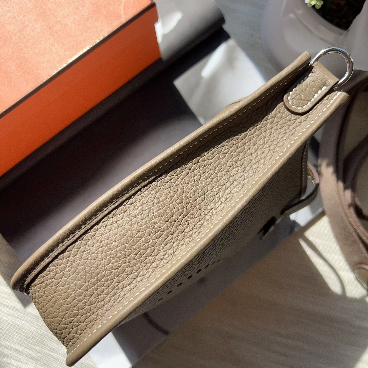 Close-up of a beige leather strap on a product with an orange box in the background.