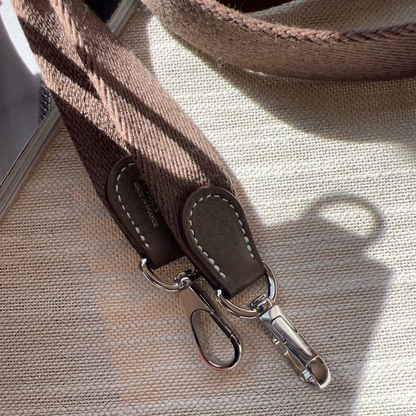 Close-up of a brown leather strap with silver buckle on a beige fabric background