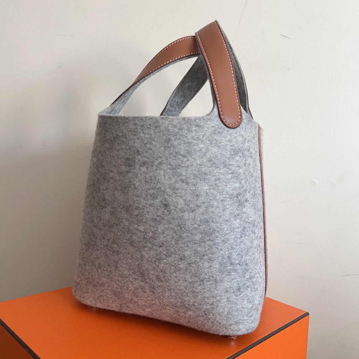Gray tote bag with brown handle on an orange surface