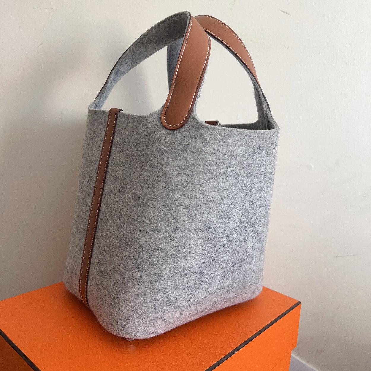 Gray tote bag with brown handles on an orange surface