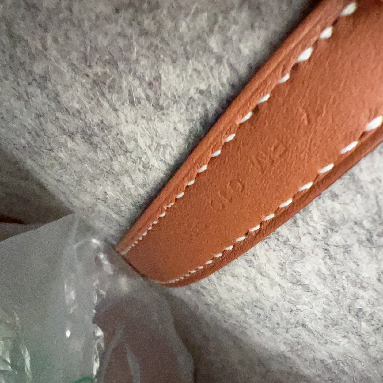 Close-up of a brown leather strap with white stitching on a textured gray surface.