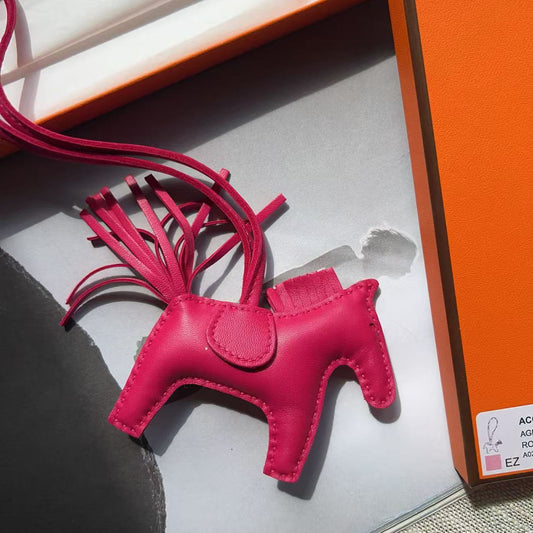 A bright pink leather accessory with a crown-like cutout and long fringed tassels, photographed inside an orange and white box. No person or real environment is present, so this is Product/Packaging rather than Lifestyle.