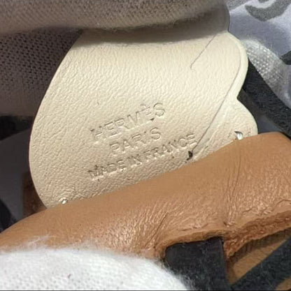 A close-up of a beige leather shoe insole with 'SEMPER SUPRA' embossed, held by white gloves next to a tan leather shoe upper with black straps.