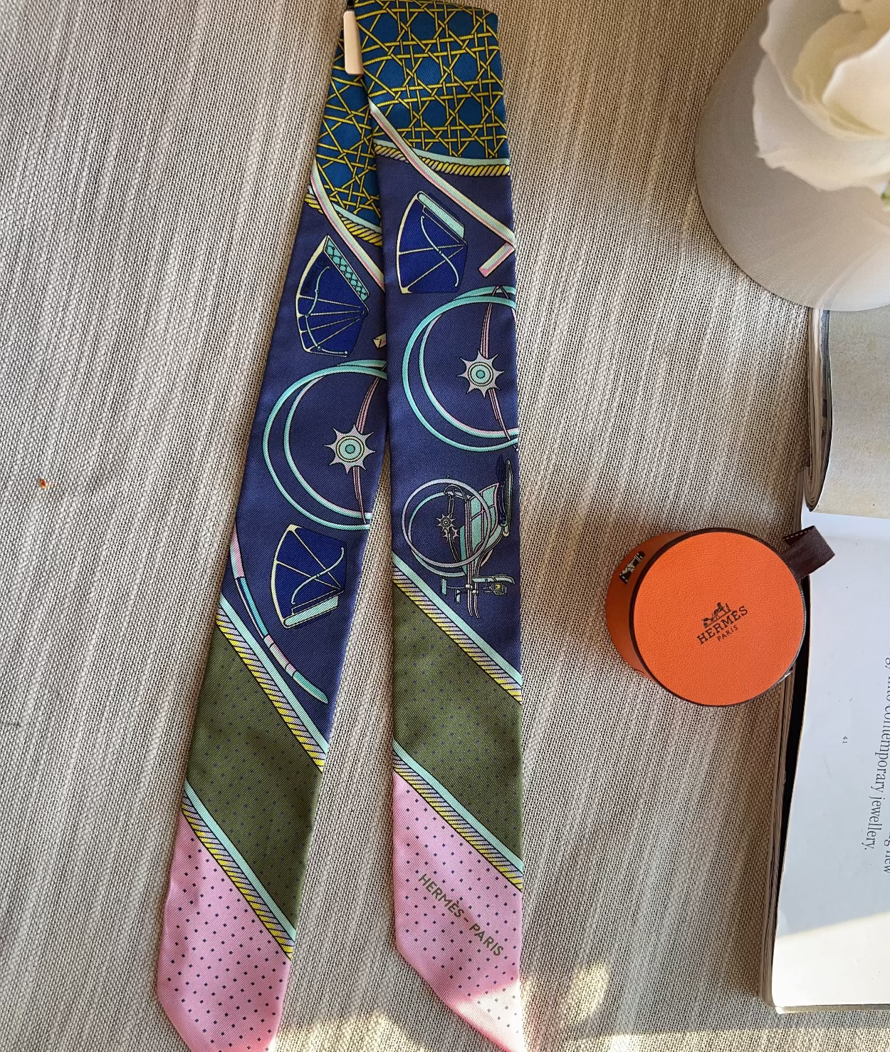Colorful patterned tie on a wooden surface with an orange round object and white flowers.