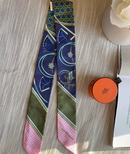 Colorful patterned tie on a wooden surface with an orange round object and white flowers.
