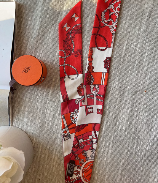Red and white patterned scarf on a textured surface with a small round container and white flowers.