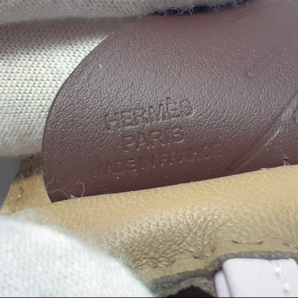 Close-up of a brown leather Hermès insole with embossed 'HERMÈS PARIS PARIS FRANCE MADE IN FRANCE' text, held by white fabric gloves.