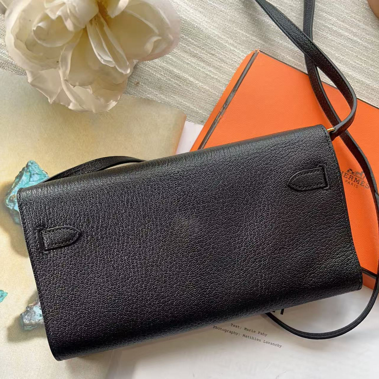 Black leather wallet on a surface with an orange book and white flower