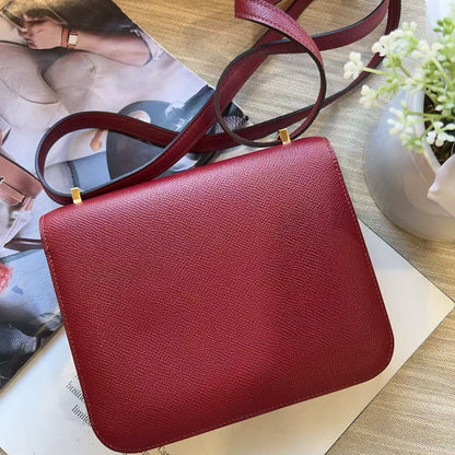 A red textured leather crossbody bag with a matching strap, styled on top of a magazine over a light wood surface.