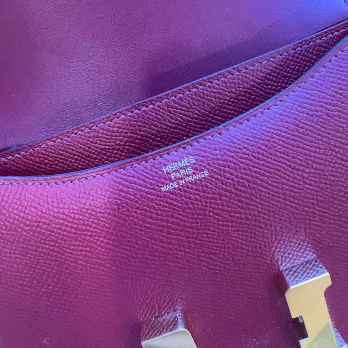 Close-up of a purple textured leather handbag showing the interior lining, stitching, and a small metal brand plaque with 'HERMÈS PARIS 14-16 AVENUE DES PALAIS-D'ARMS'.