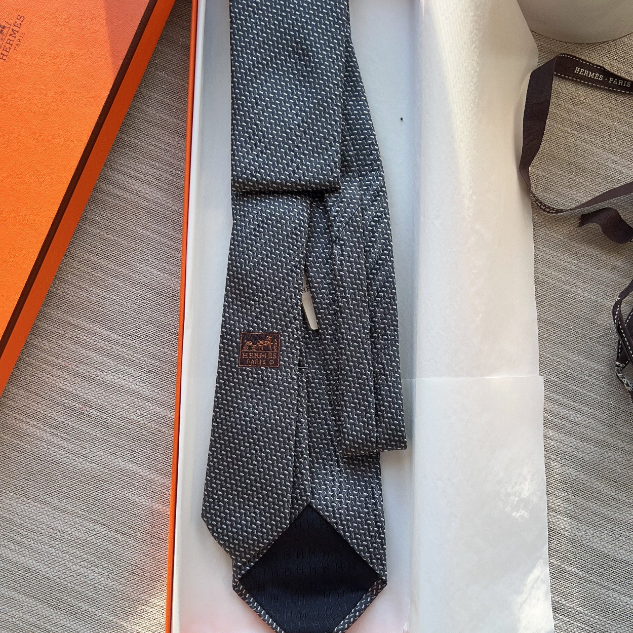 Gray patterned tie in an open orange and white box on a textured surface.