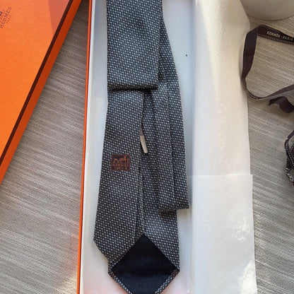 Gray patterned tie in an open orange and white box on a textured surface.
