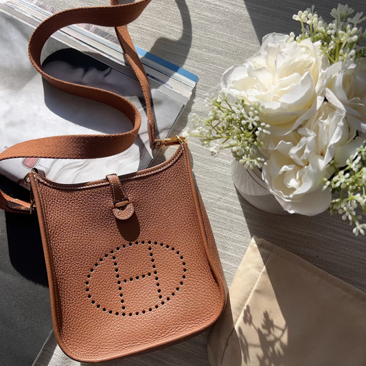 Brown leather handbag with a visible brand logo on a light surface with flowers and papers.