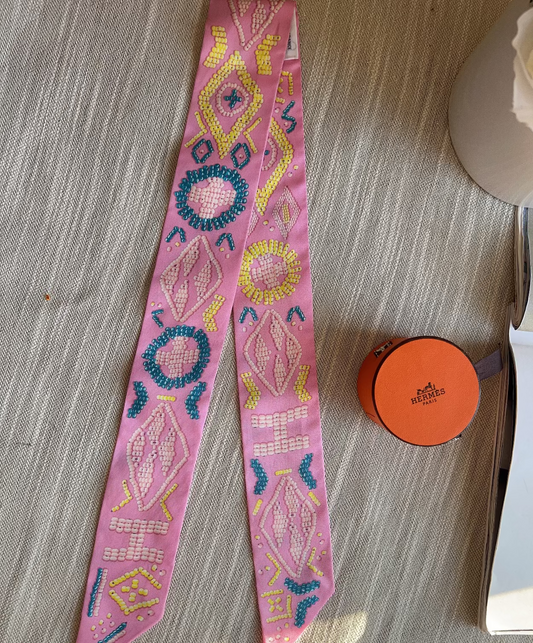 Decorative pink ribbon with bead patterns on a textured surface next to a small orange container.