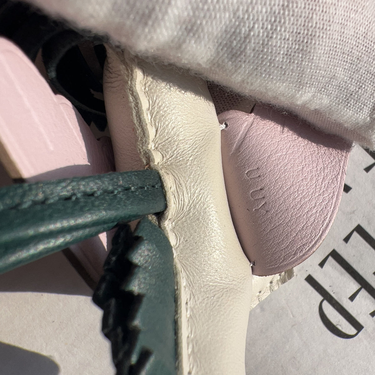 A close-up of a light pink leather shoe insert or insole with the brand name 'mum' embossed on it, partially covered by a white fabric sleeve. A dark green leather strap is visible on the left, and the word 'DEEP' is printed on a light-colored surface in the background.