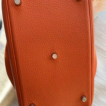 Close-up of an orange leather bag with metal studs on a light background