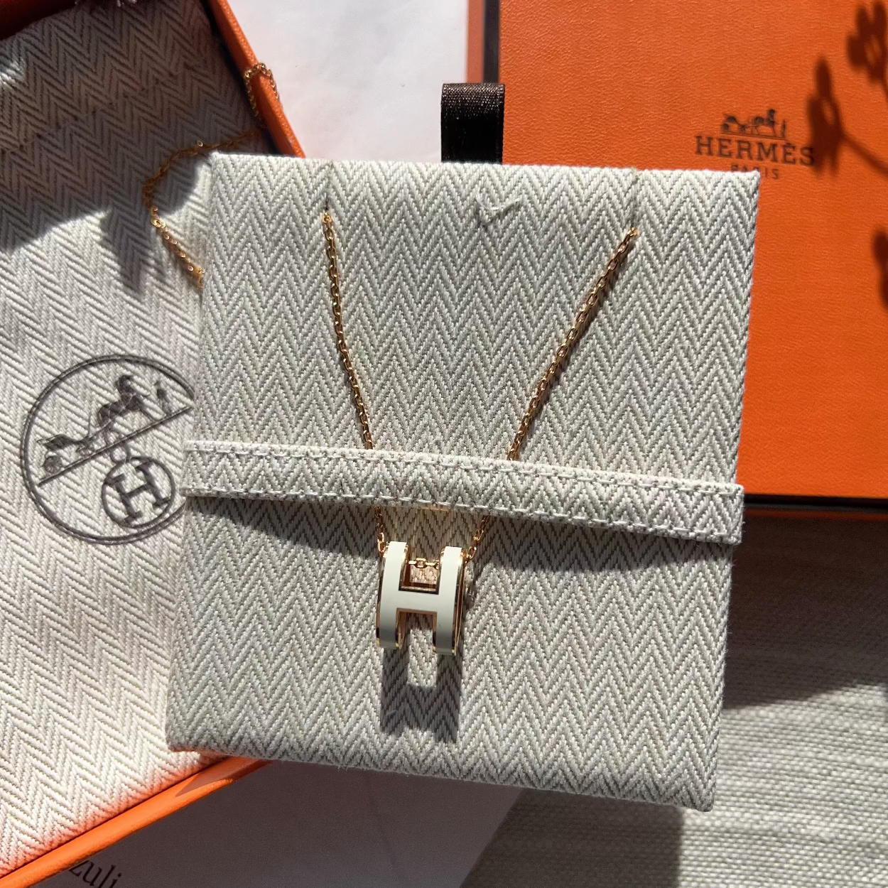 Gray textured handbag with gold 'H' emblem on a surface with orange and gray background