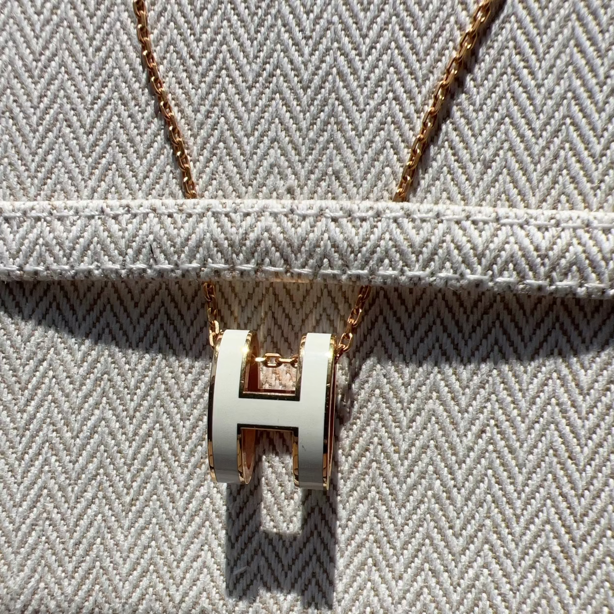 Gold necklace with a 'H' pendant on a textured surface