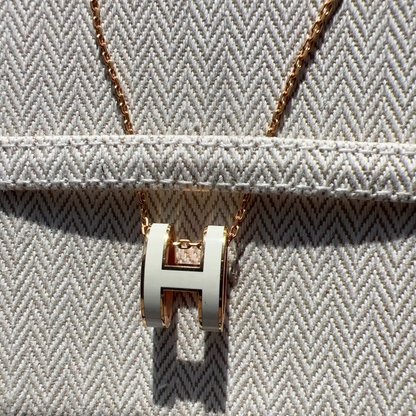 Gold necklace with a 'H' pendant on a textured surface