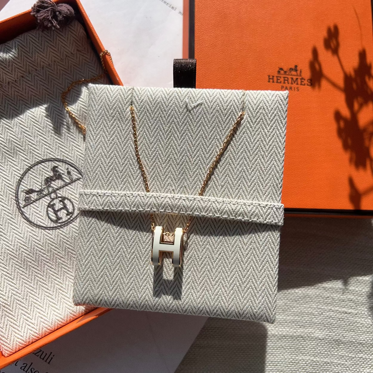 Small rectangular handbag with gold clasp on a textured surface with Hermès branding.