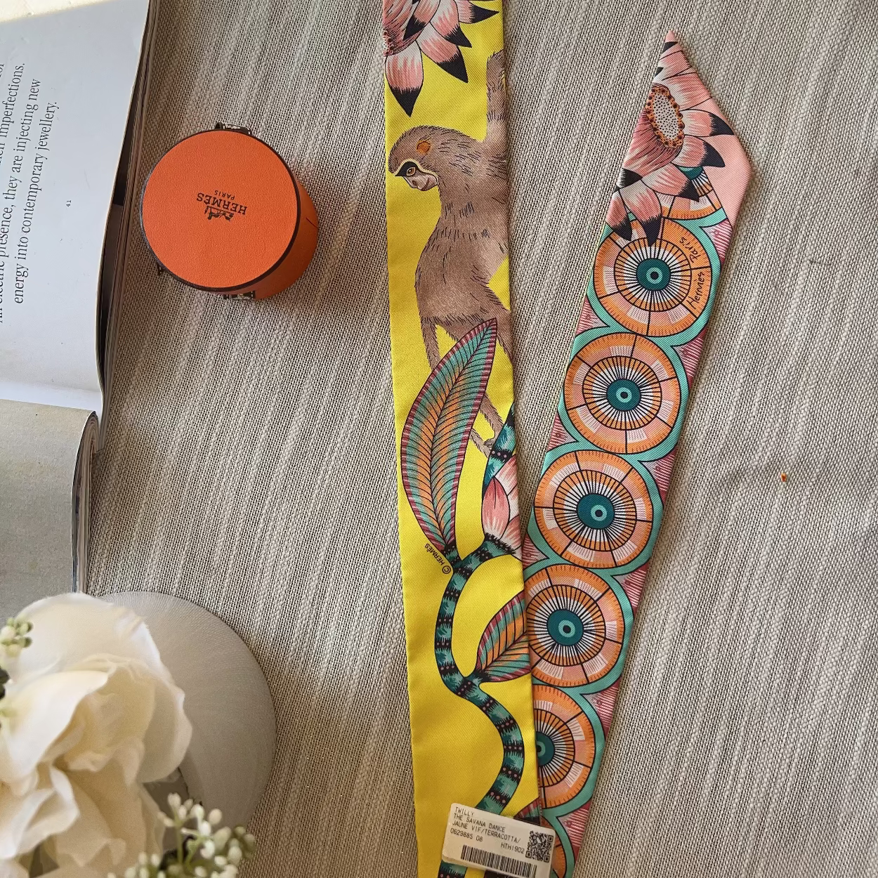 Decorative belt with floral patterns on a wooden surface next to an open book and small round object.