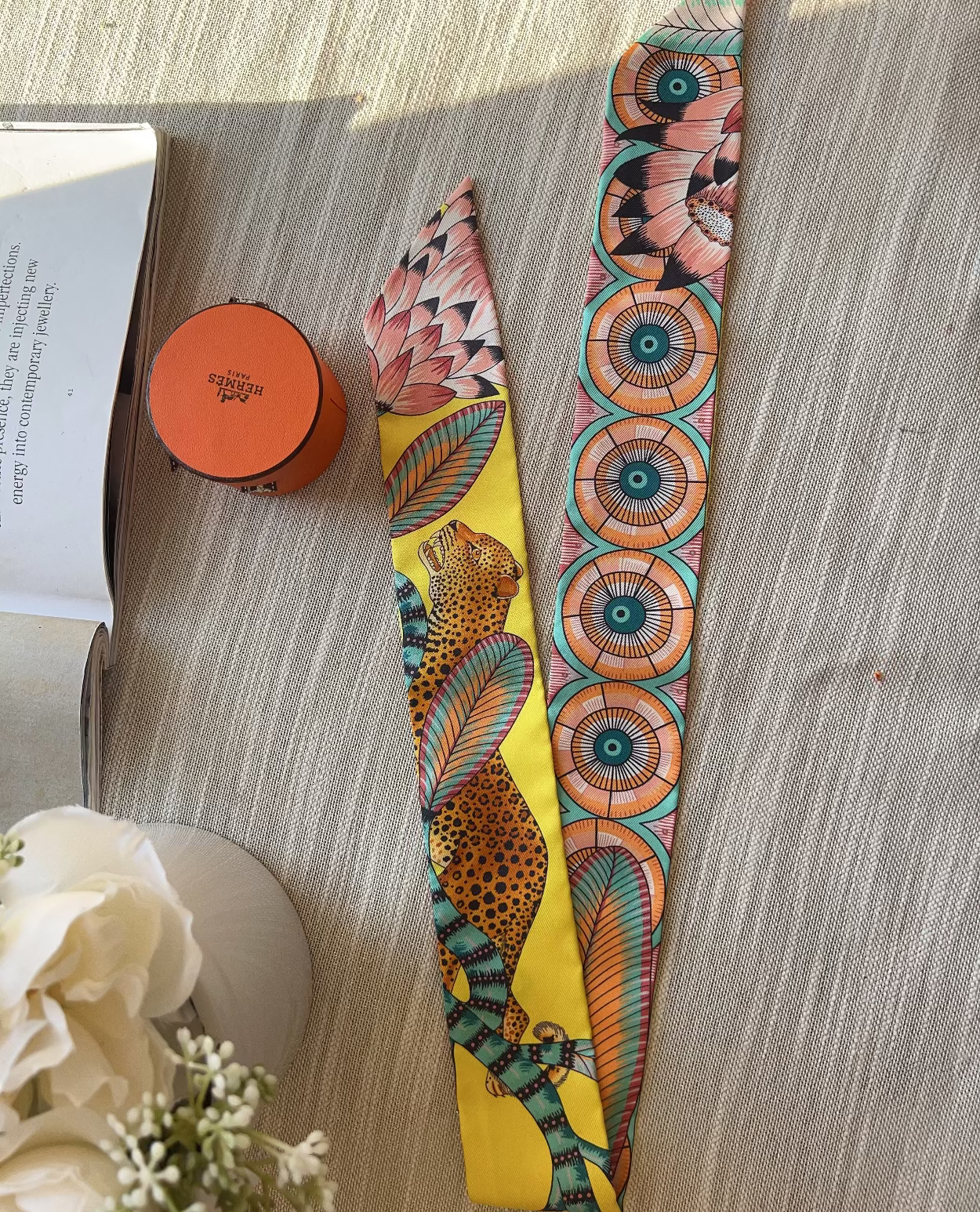 Colorful patterned belt on a wooden surface with a book and small container in the background.