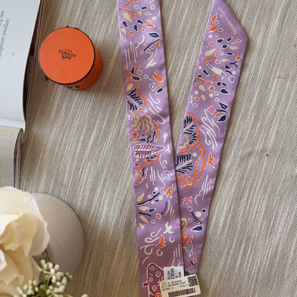 Two purple patterned hairbands on a textured surface with an orange container and white flowers in the background.