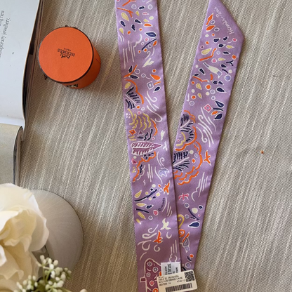 Two purple patterned hairbands on a textured surface with an orange container and white flowers in the background.