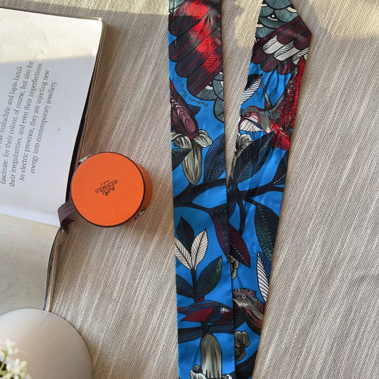 Floral-patterned tie on a wooden surface with an open book and orange object.
