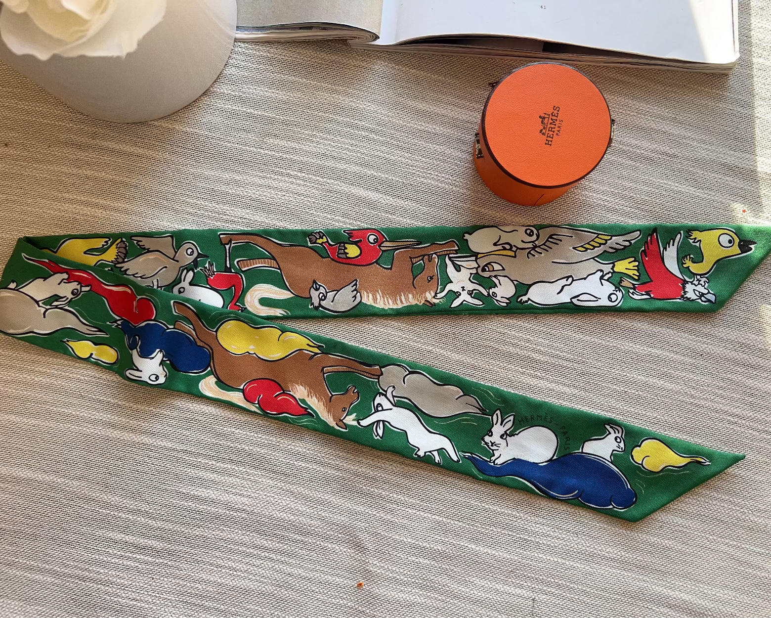 Colorful animal-themed ribbon on a wooden surface with a white vase and orange container in the background.