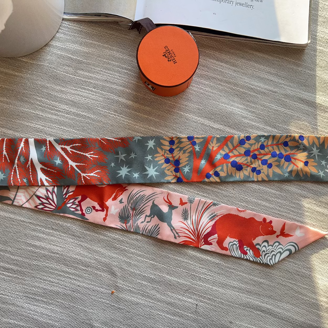 Two colorful fabric scarves on a wooden surface with a small round object and book in the background.