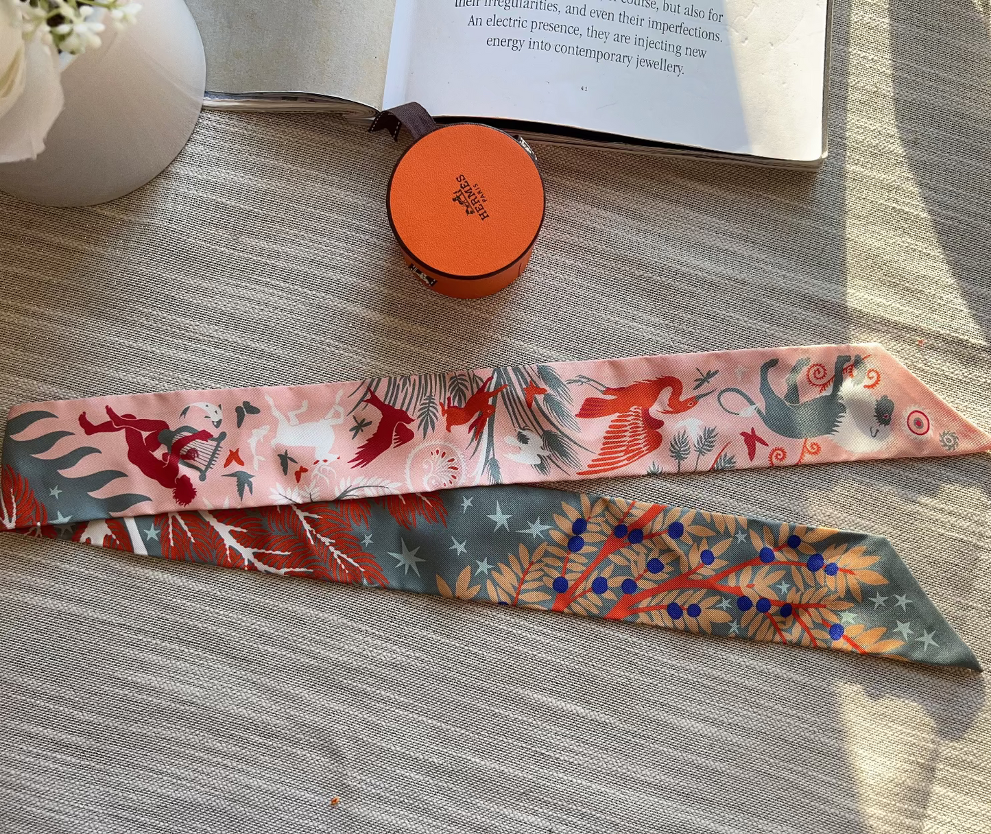 Two colorful patterned scarves on a wooden surface with a small container and book in the background.