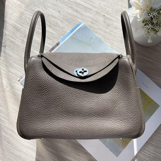 Brown leather handbag with a decorative clasp on a textured surface with flowers.