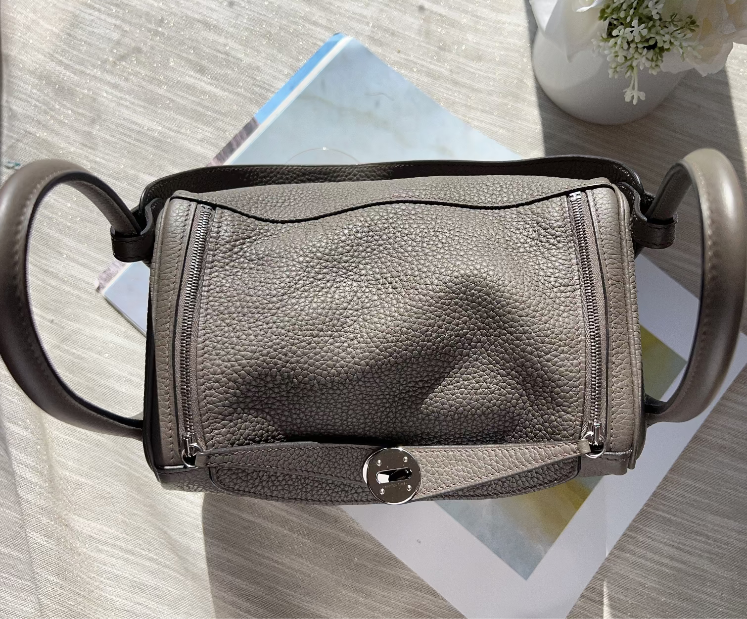 Gray leather handbag with black handles on a light wooden surface.