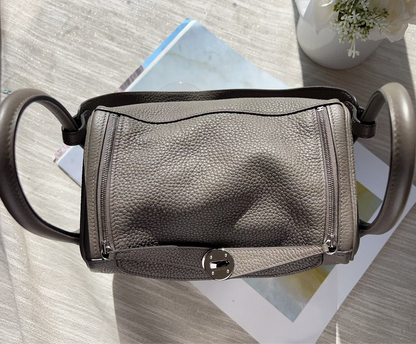Gray leather handbag with black handles on a light wooden surface.
