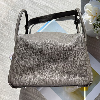 Small gray leather bag on a textured surface with flowers and a magazine in the background
