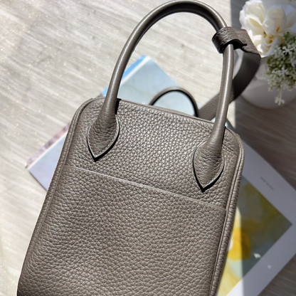 Gray leather handbag on a light wooden surface with a tablet and flowers.