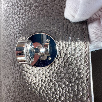 Close-up of a textured gray leather surface with a silver circular emblem and a white glove partially covering it.