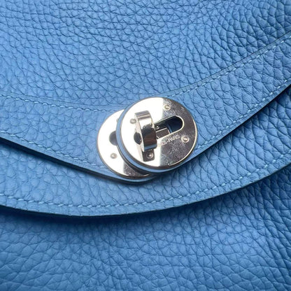 Close-up of a blue pebbled leather handbag with a silver metal turn-lock closure on a curved strap.