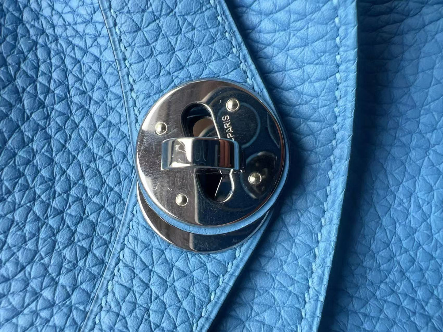 Close-up of a light blue textured leather bag with a polished silver-tone metal clasp.